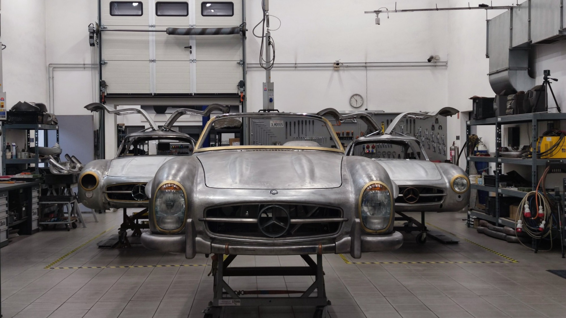 Three bare-metal 300 SL bodies in the workshop, a roadster in the middle and two Gullwing coupés with open doors