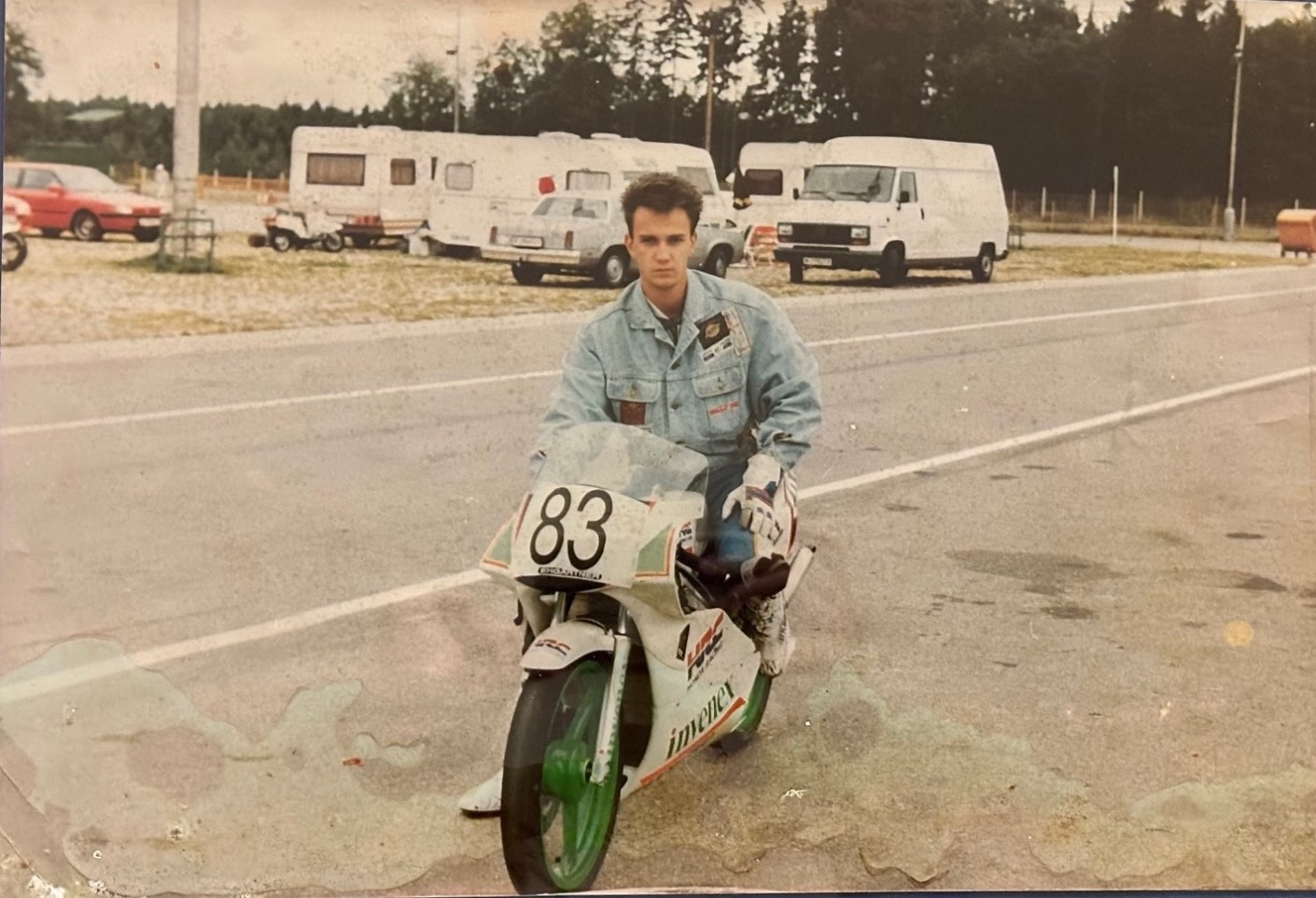 Zsolt Nagy as a young racer, kneeling behind his white and green racing motorcycle, number 83, on a race track