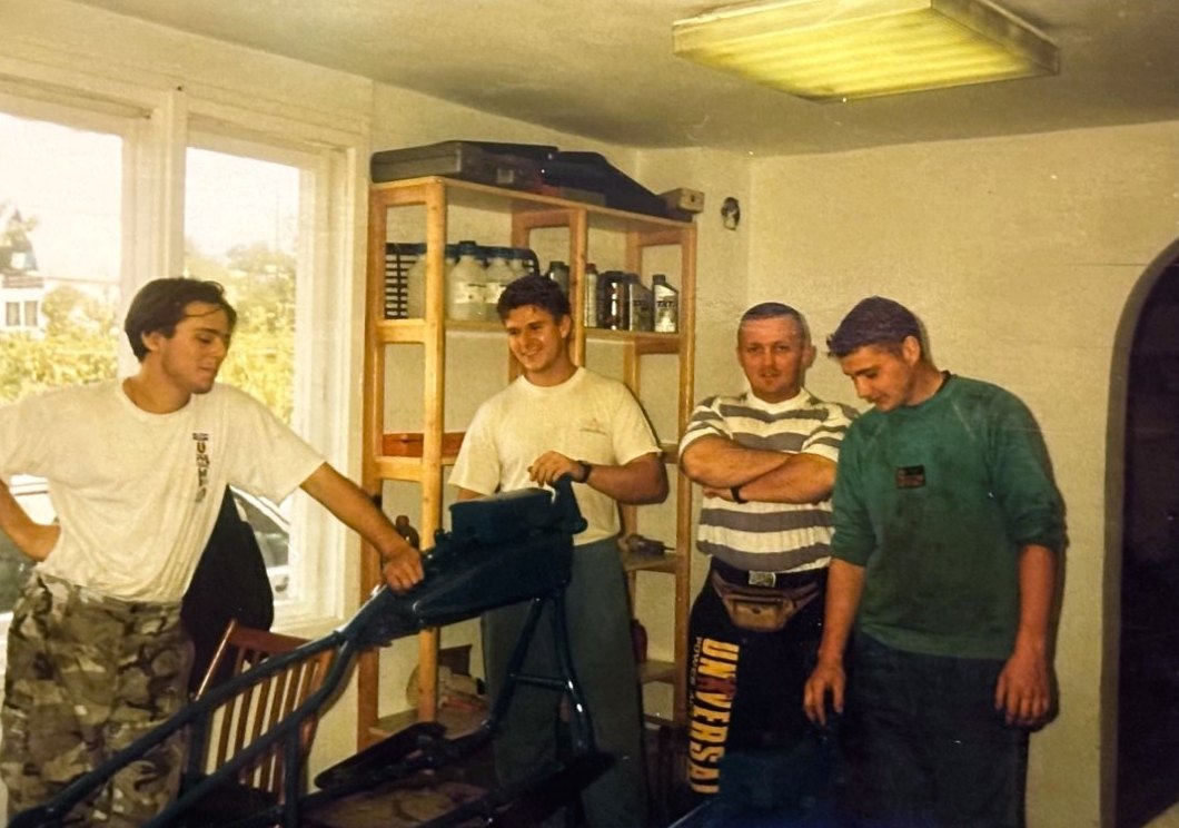 Four people around a motorcycle frame in the workshop