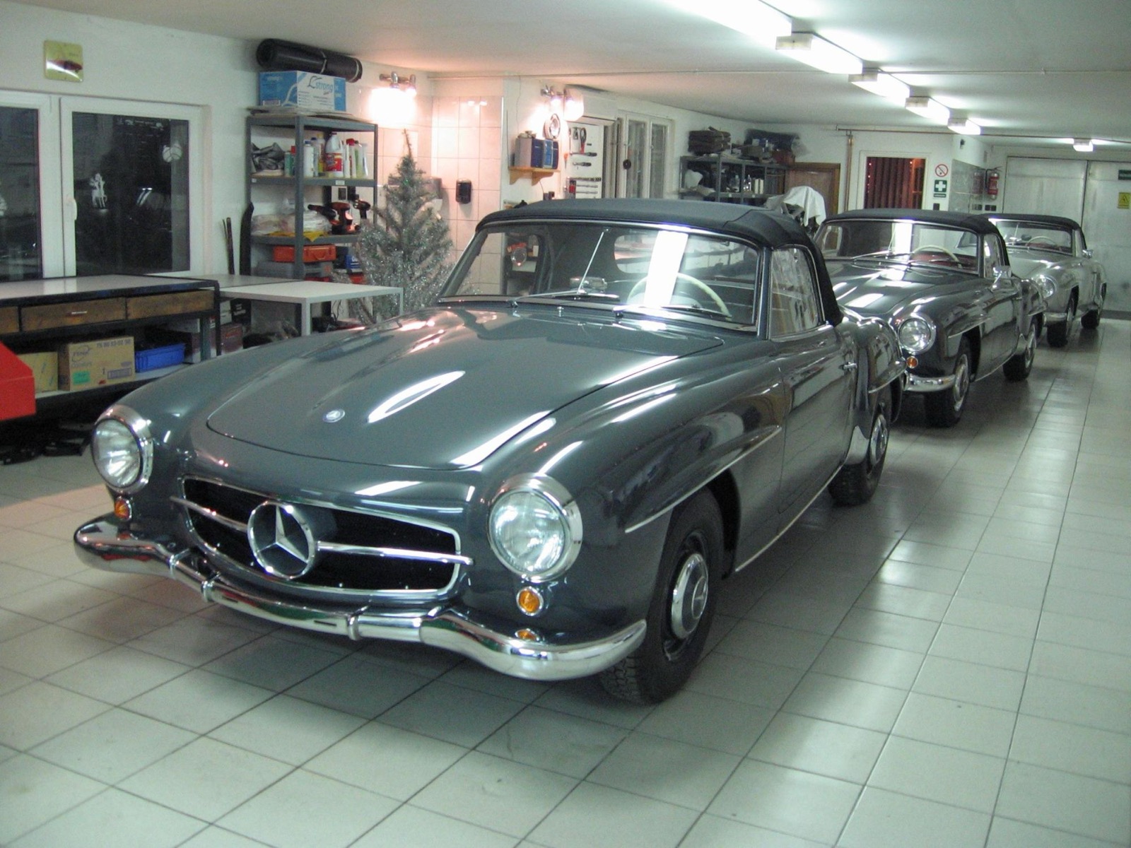 A grey Mercedes-Benz 190 SL in the old garage, with two more 190 SLs behind it