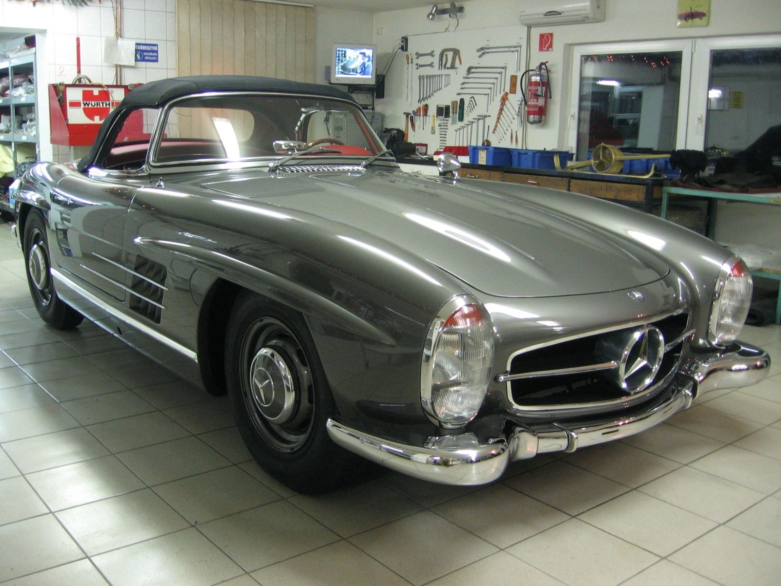 A grey Mercedes-Benz 300 SL Roadster with a black soft top in the old garage