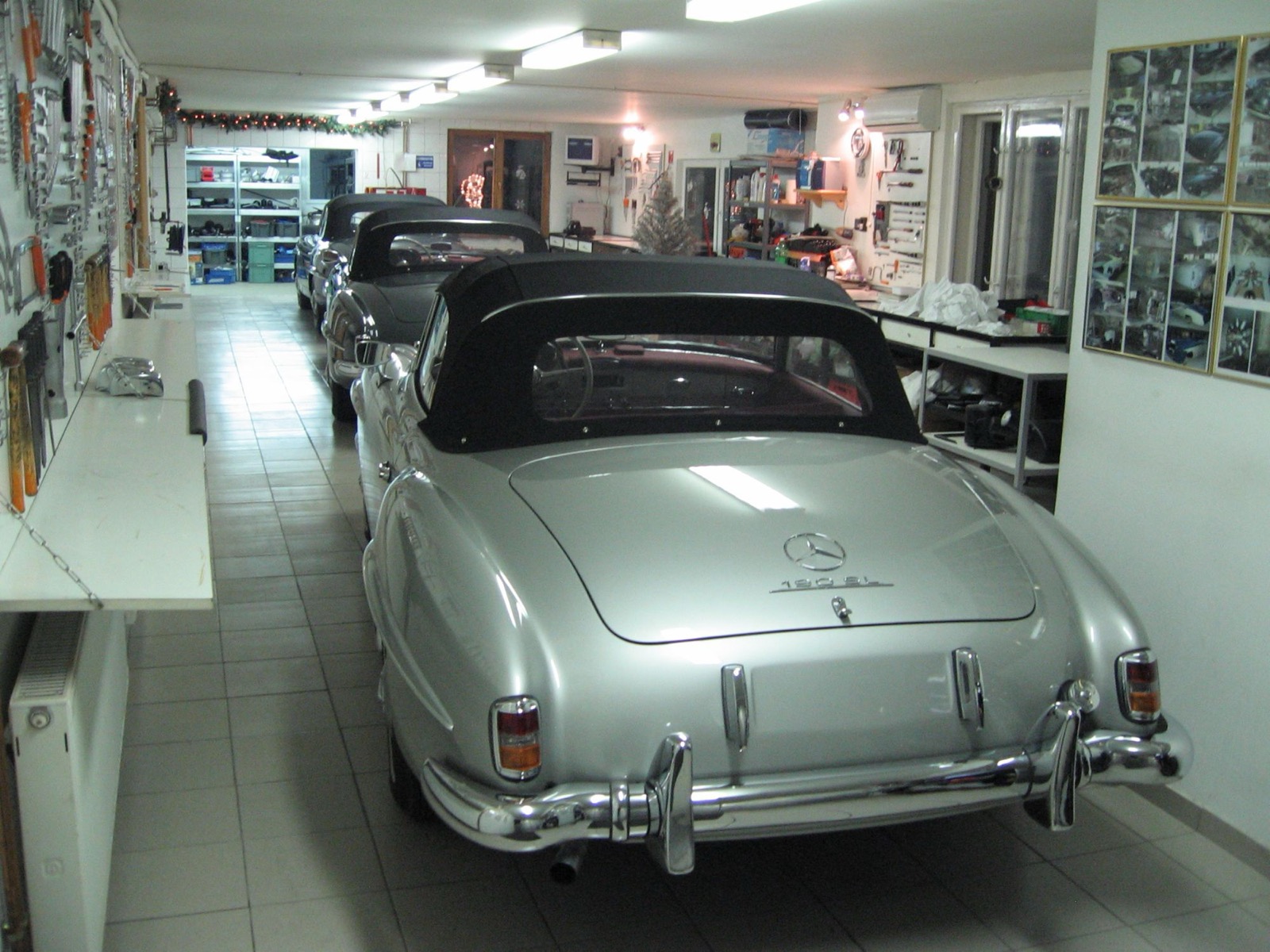 A silver Mercedes-Benz 190 SL seen from the rear in the old garage, with more cars lined up behind it