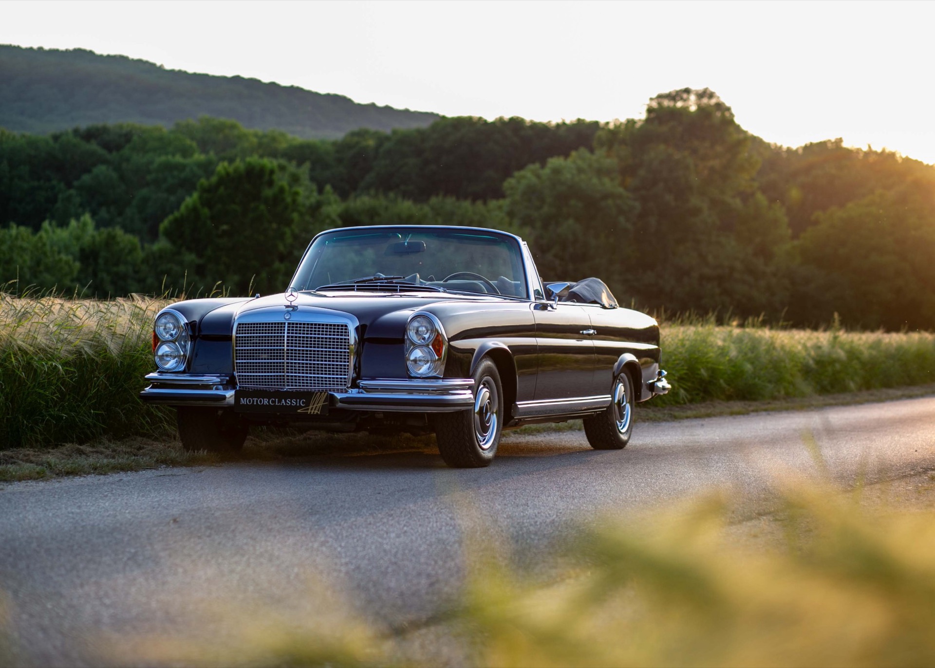 Dark blue Mercedes-Benz W111 convertible parked on a country road at sunset