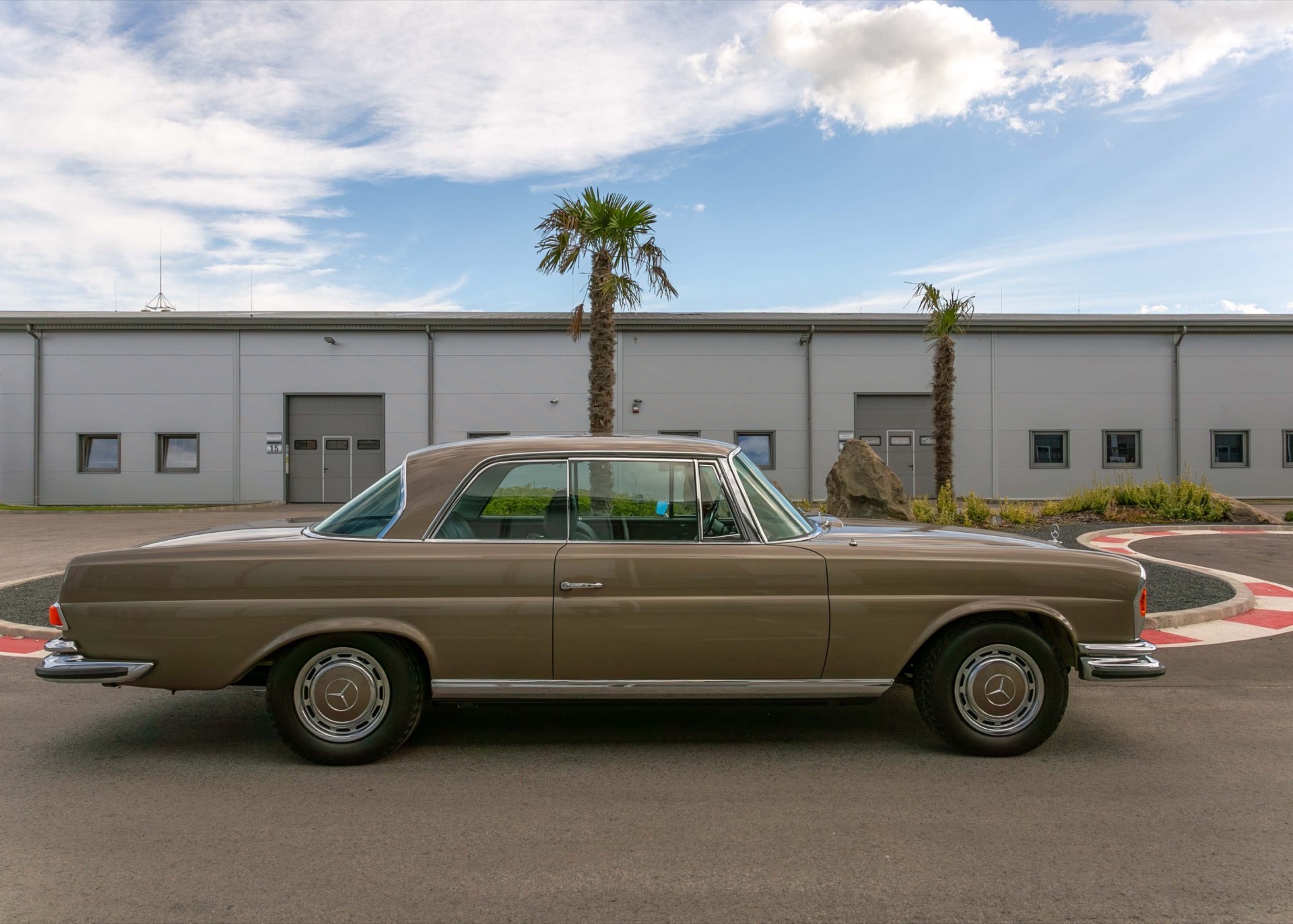 Mercedes-Benz W111 coupé in brown, side view in front of a hall with palm trees
