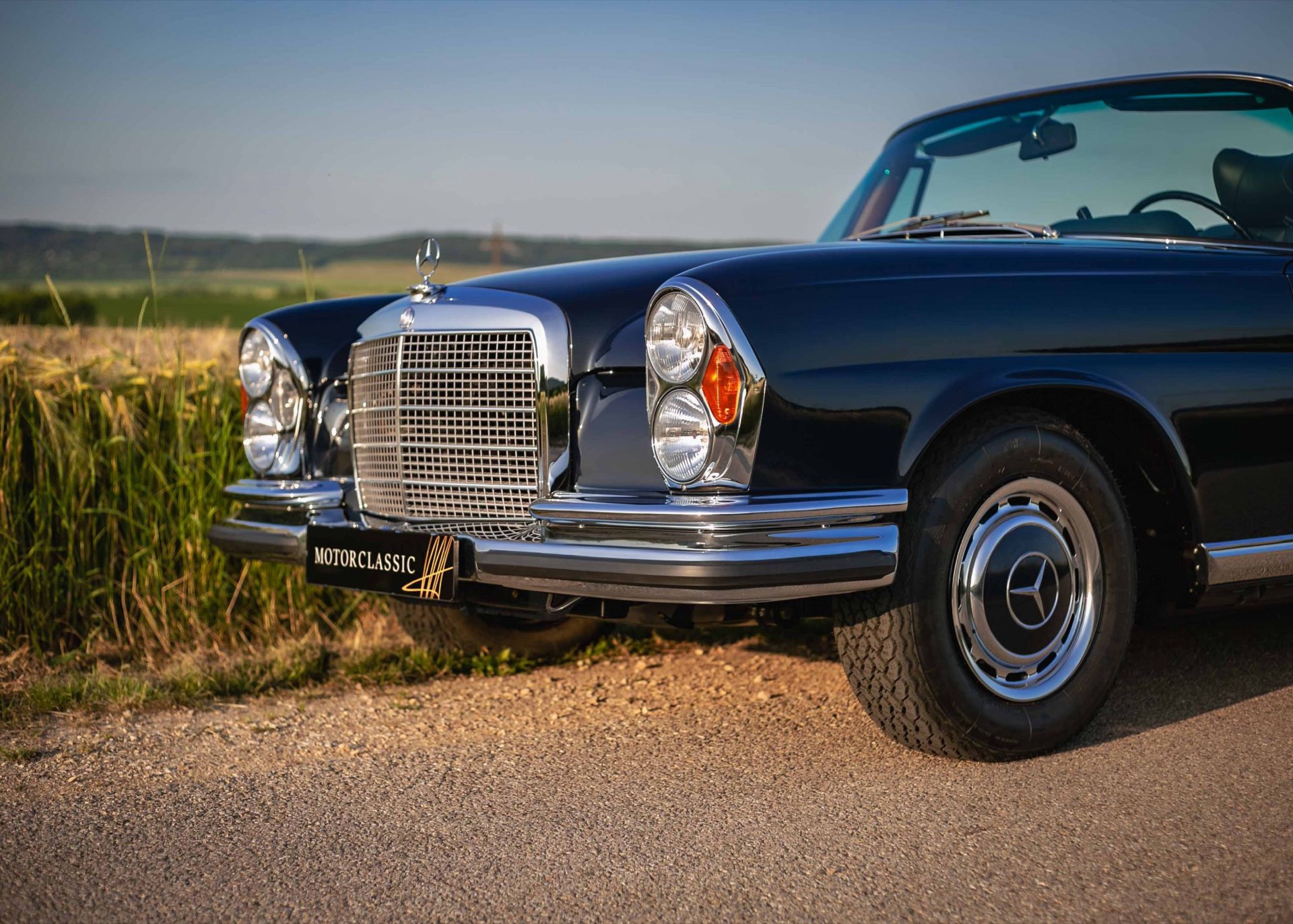 Front of a dark blue W111 convertible with chrome bumpers, twin headlamps and the Motor Classic plate