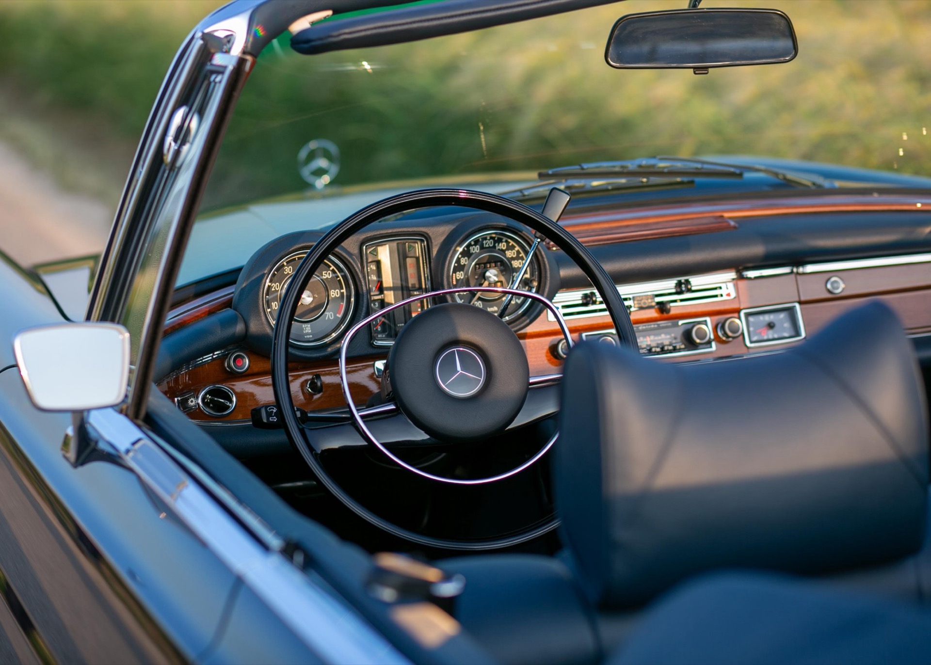 Steering wheel and wooden dashboard of a W111 convertible, seen from the driver's door with the road ahead